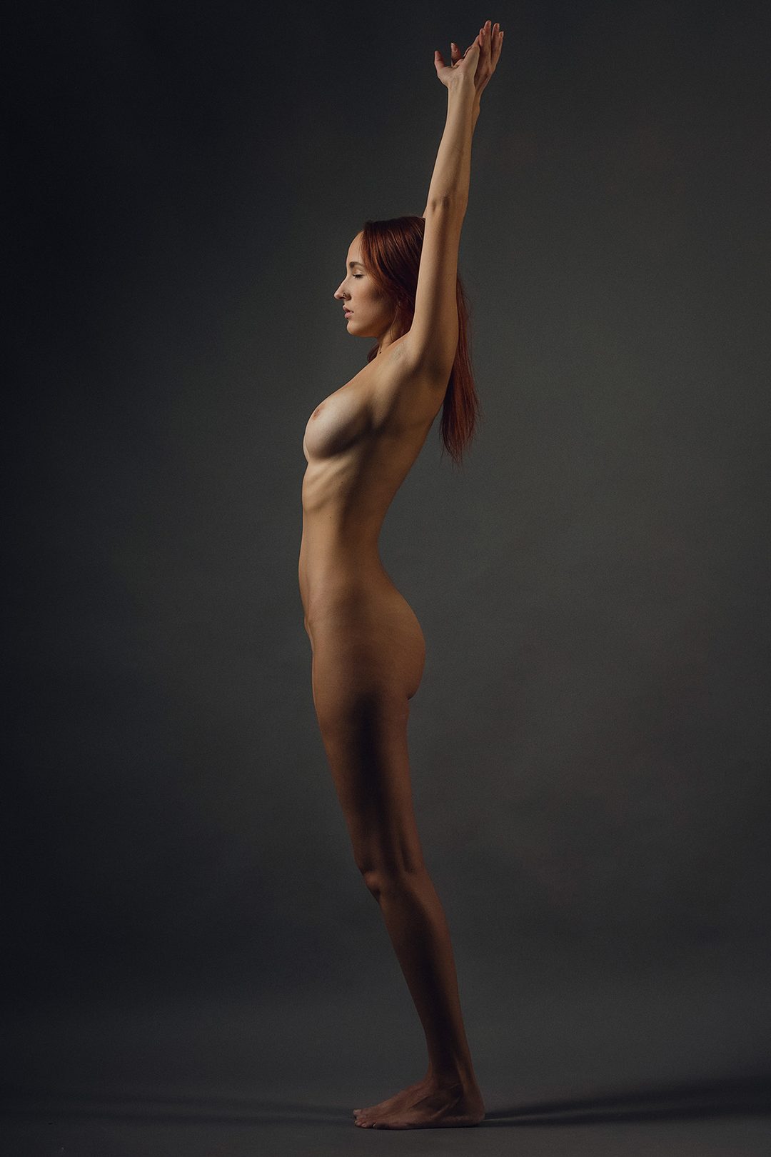 Künstlerischer Studioakt der Modelin Lucia, stehend im Profil mit erhobenen Armen, Bratislava, Slowakei, 2018.